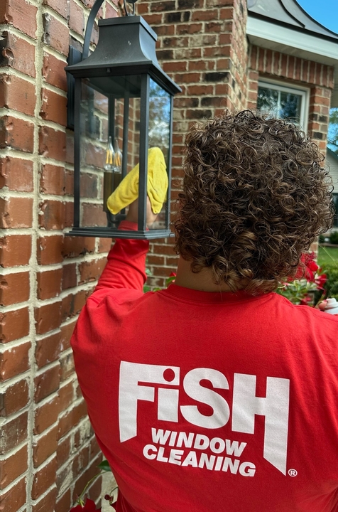 FISH professional cleaning an exterior coach light on a brick home