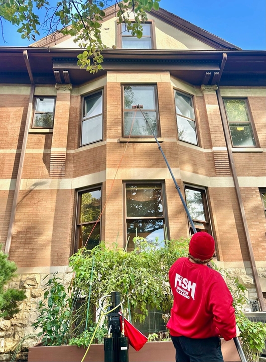 Local FISH technician cleaning upper-story windows on a brick Chicago-area home