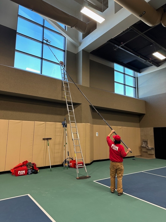 Local FISH technician cleaning tall interior facility windows